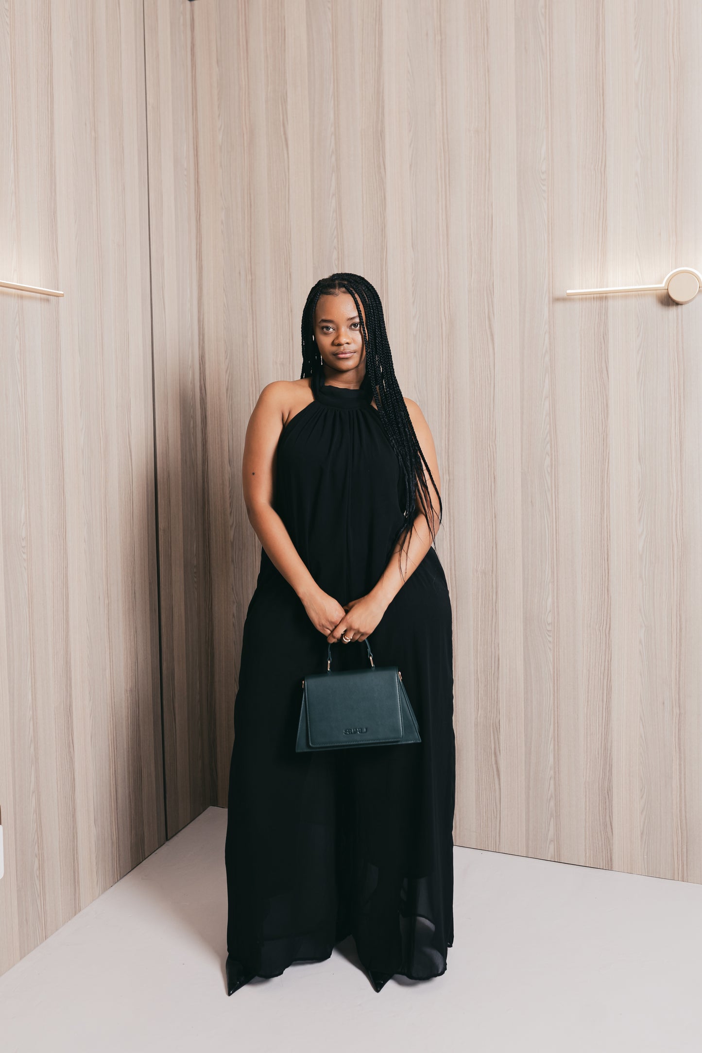 Woman in a black dress holding a green SUHU handbag against a neutral background
