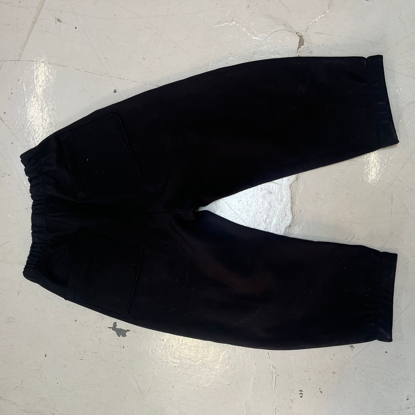 Black wide-leg cropped pants with an elastic waistband, laid flat on a light gray concrete floor.