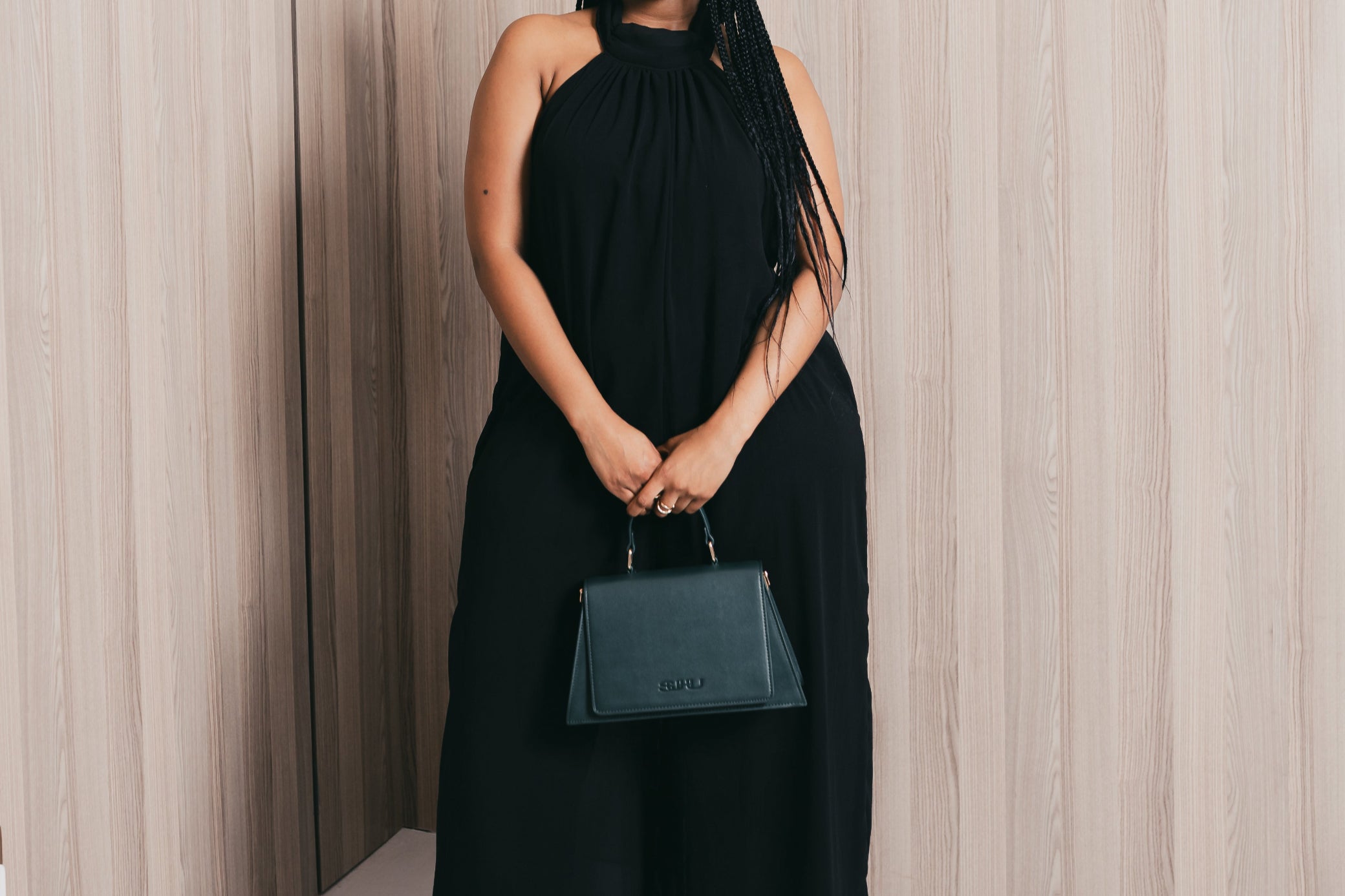 Woman in a black dress holding a Forest green SUHU handbag against a neutral background