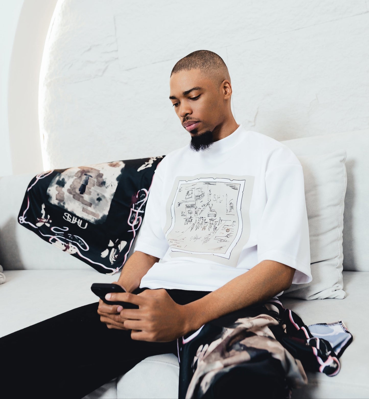 SUHU Model sitting on a white couch using a phone with a white wall and decorative elements in the background