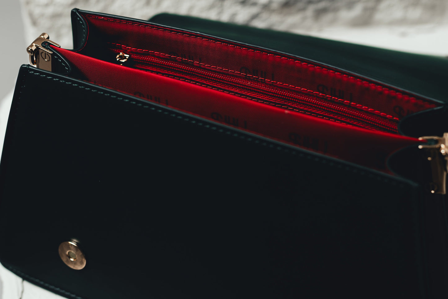 Forest handbag with gold accents and red interior against a textured white background