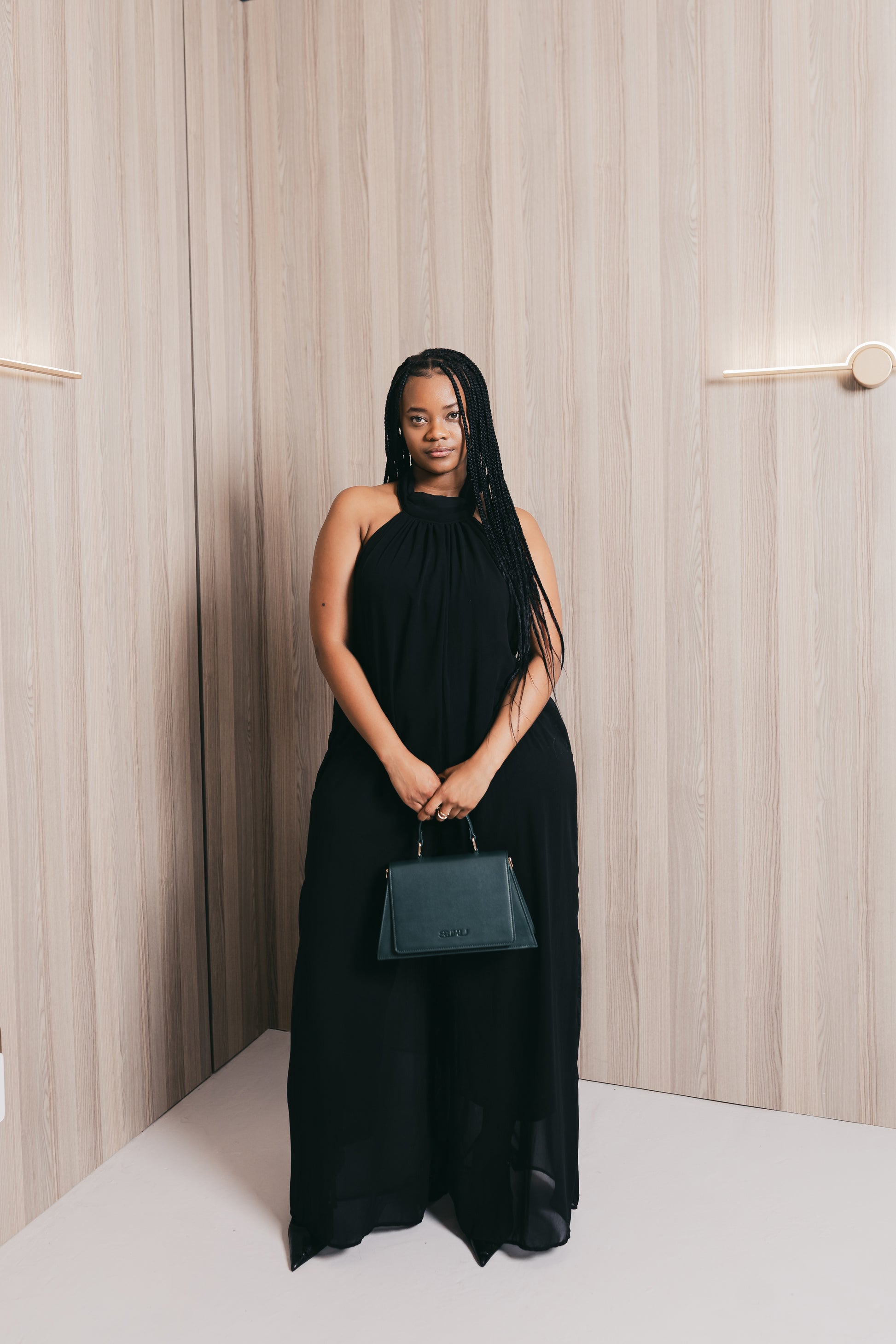 Woman in a black dress holding a green SUHU handbag against a neutral background