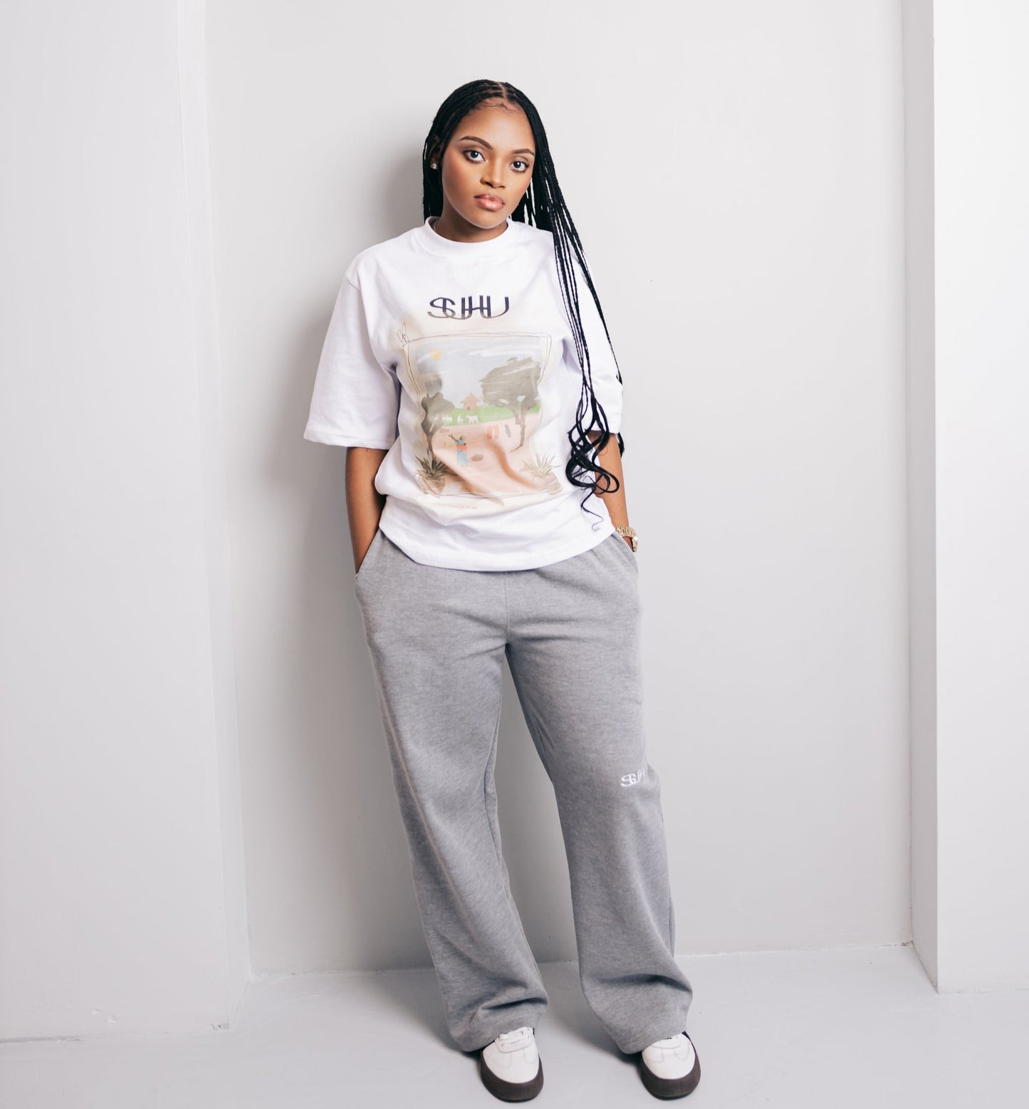Model wearing a white SUHU t-shirt with graphic design and gray sweatpants against a white background
