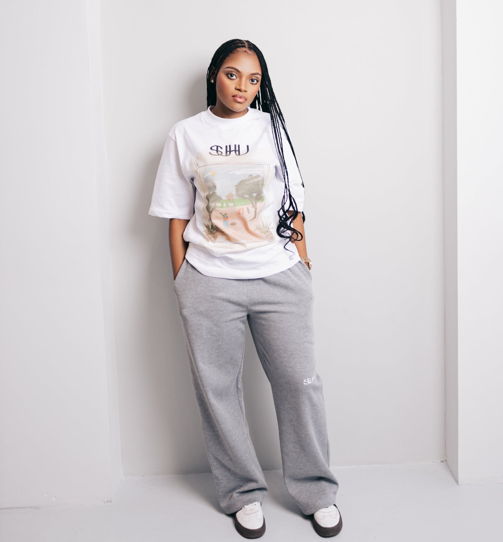 Model wearing a white SUHU t-shirt with graphic design and gray sweatpants against a white background