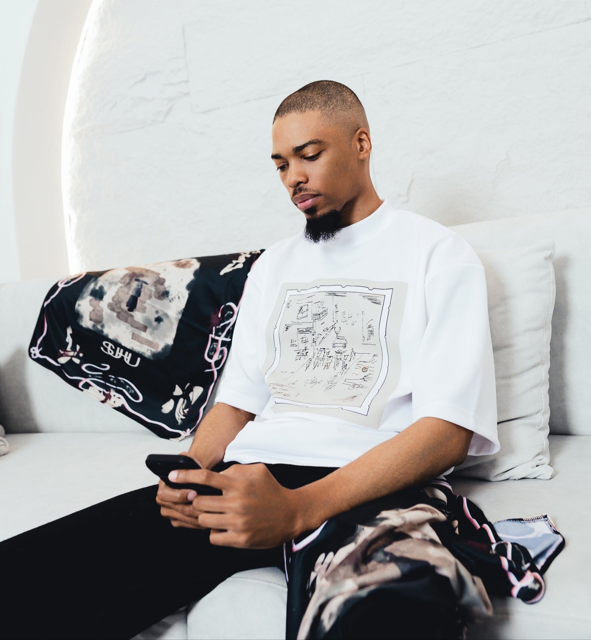 SUHU Model sitting on a white couch using a phone with a white wall and decorative elements in the background