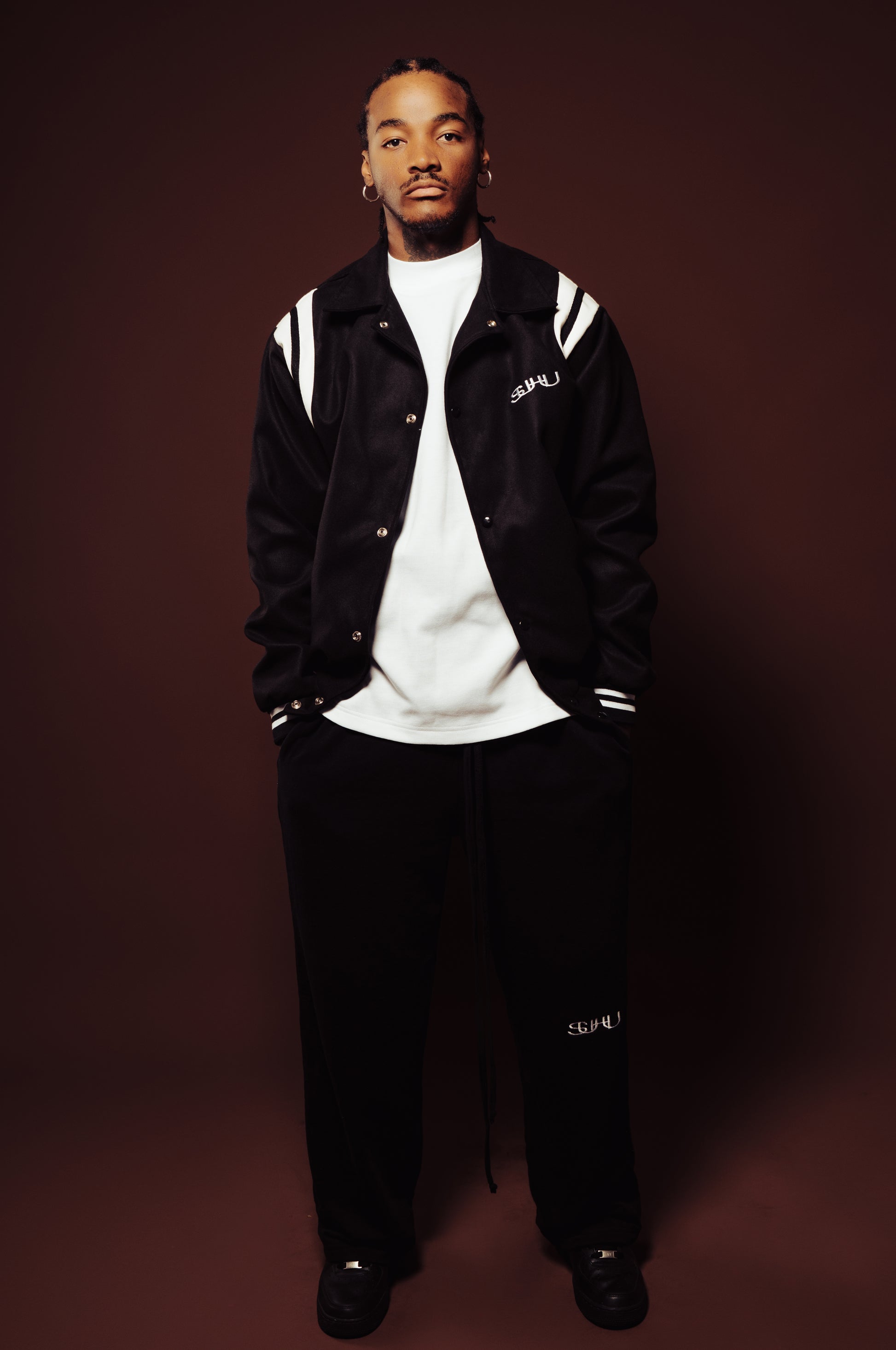 Man wearing a black jacket with white accents and a white shirt against a dark background